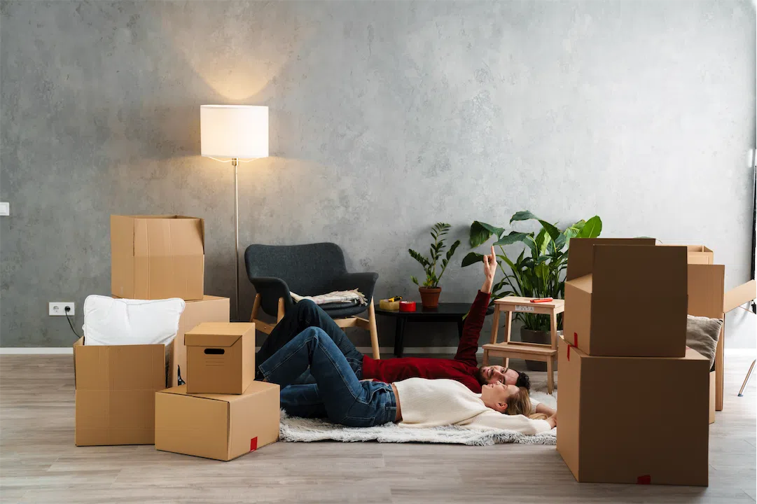 A young couple rests among moving boxes, planning the next steps in their home buying journey.